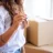 young-woman-showing-giving-key-posing-new-apartment-with-heap-carton-boxes-background